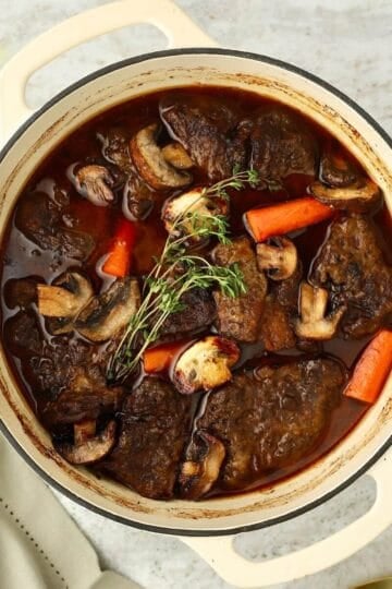 Braised chuck roast with a red wine sauce, carrots and mushrooms in a white Dutch oven.