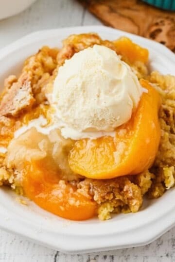 A big bowl with a serving of peach cobbler topped with a scoop of vanilla ice cream.