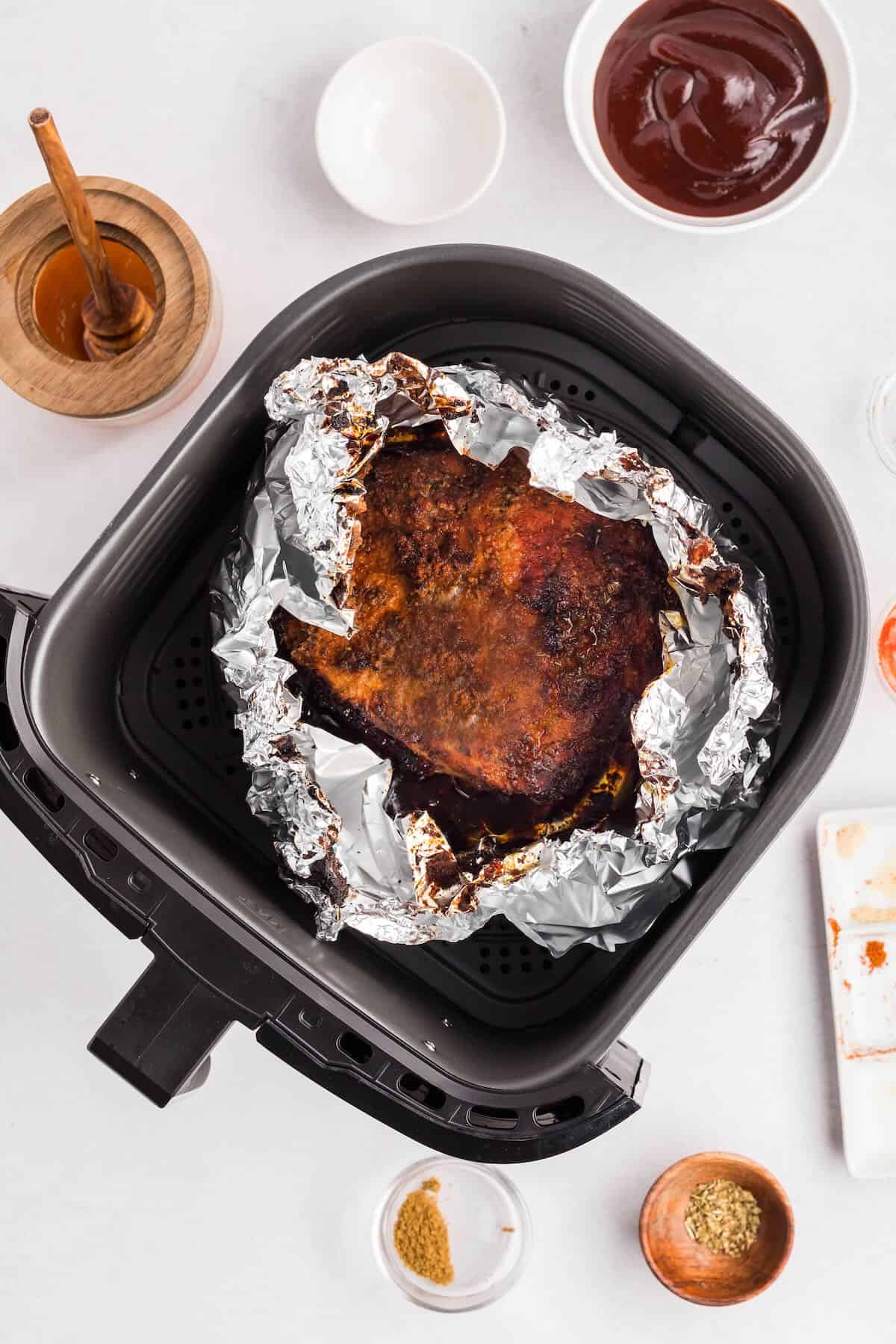 Partially cooked Boston butt wrapped in foil in an air fryer basket. 