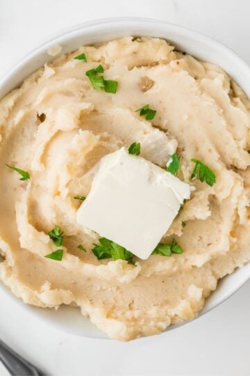 A white bowl full of whipped crock-pot mashed potatoes topped with a pat of butter.