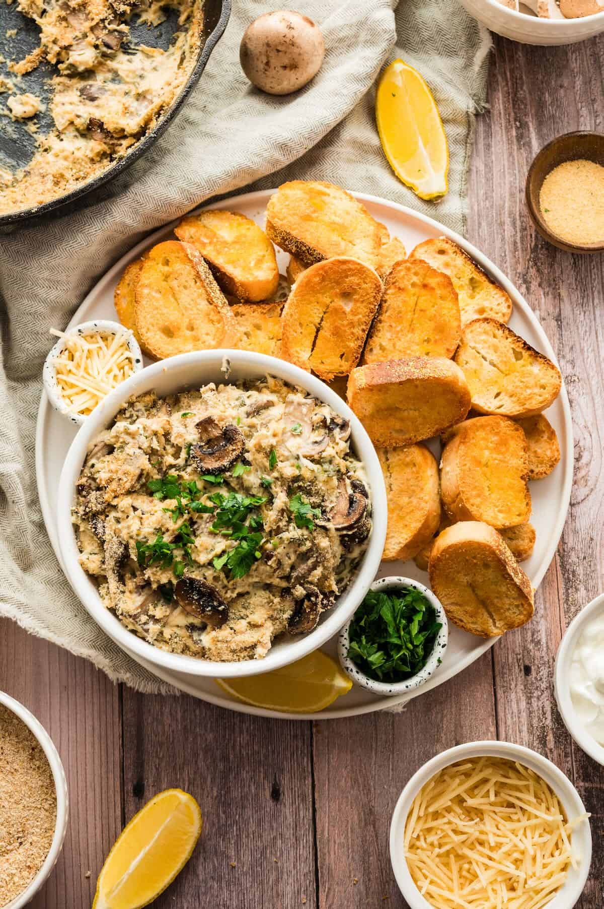 Mushroom dip in a bowl on a plate with toasted crostini.