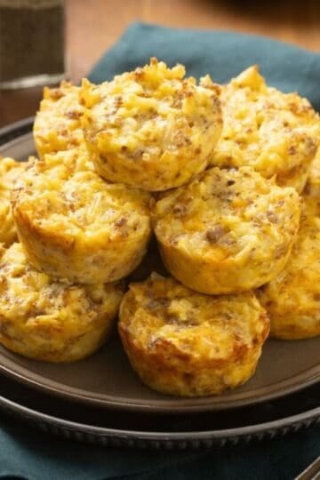 A stack of sausage, egg, cheese, and hash brown breakfast muffins on a plate.