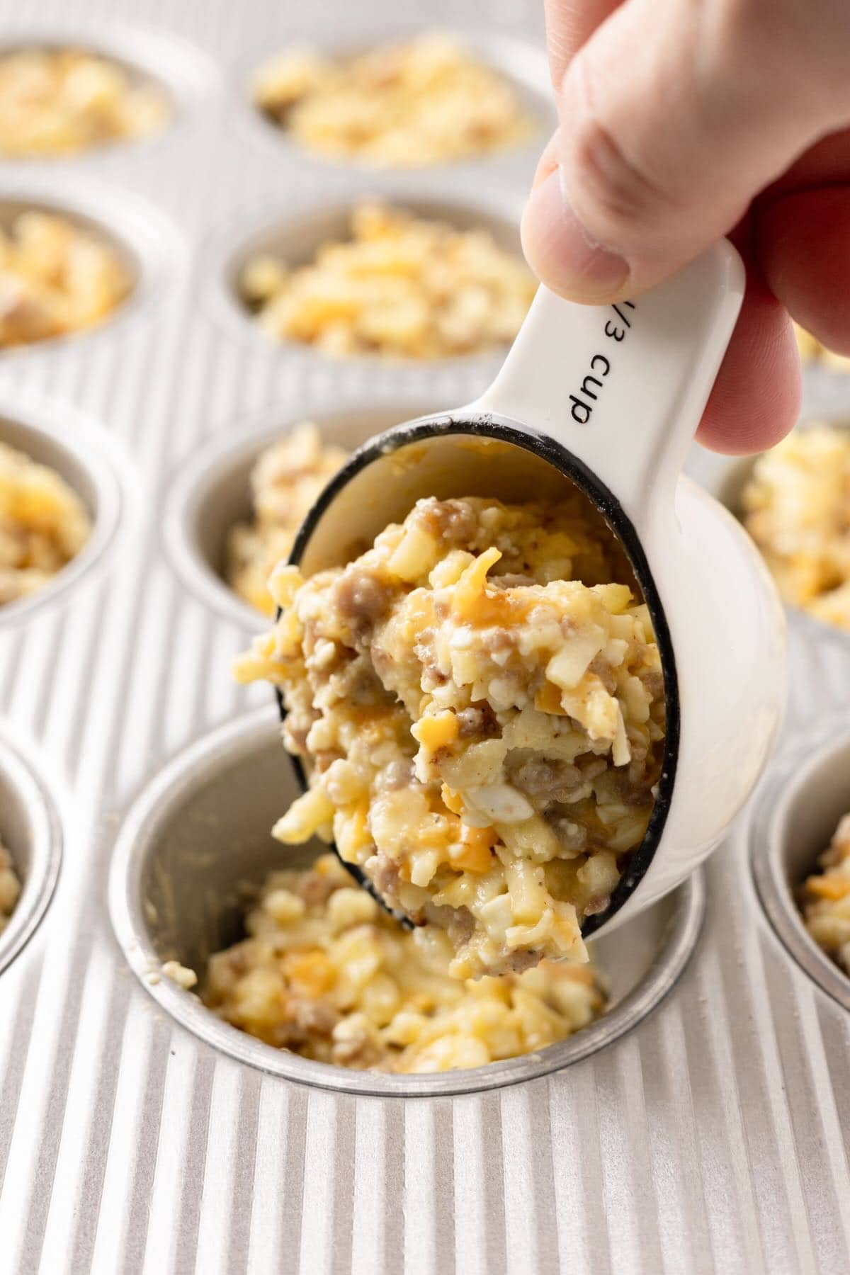 Filling muffin pan cups with breakfast muffins mixture before baking. 