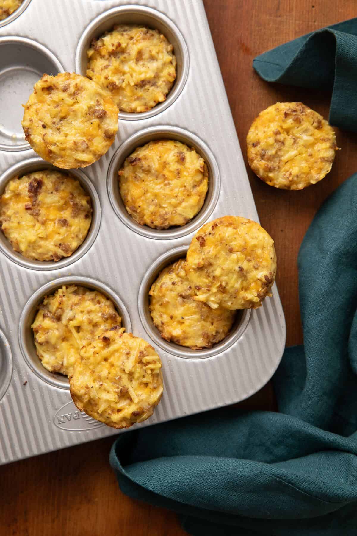 Baked sausage, egg, cheese, and hash brown muffins being removed from a muffin pan. 