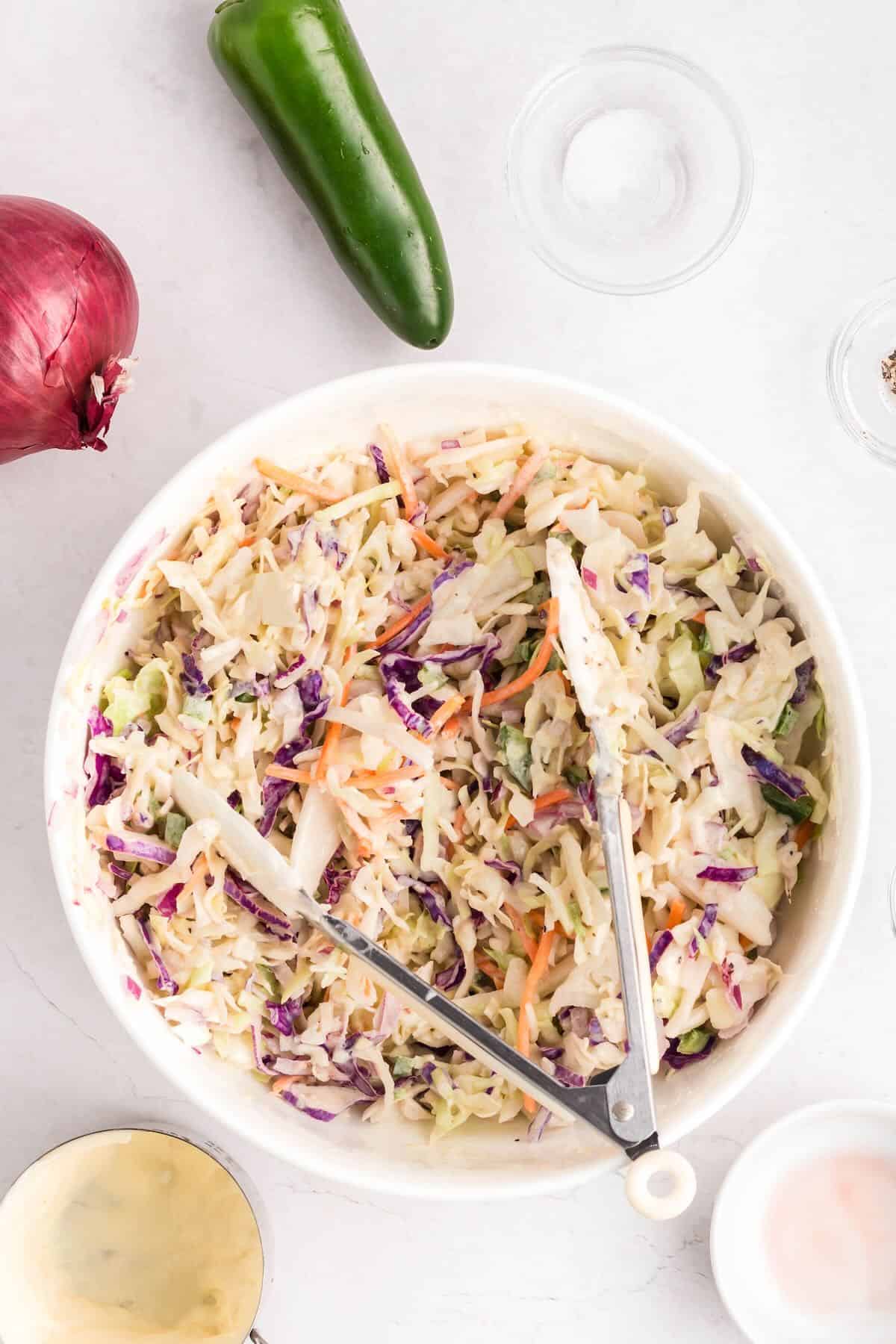A large bowl of coleslaw with tongs to toss the slaw and dressing. 
