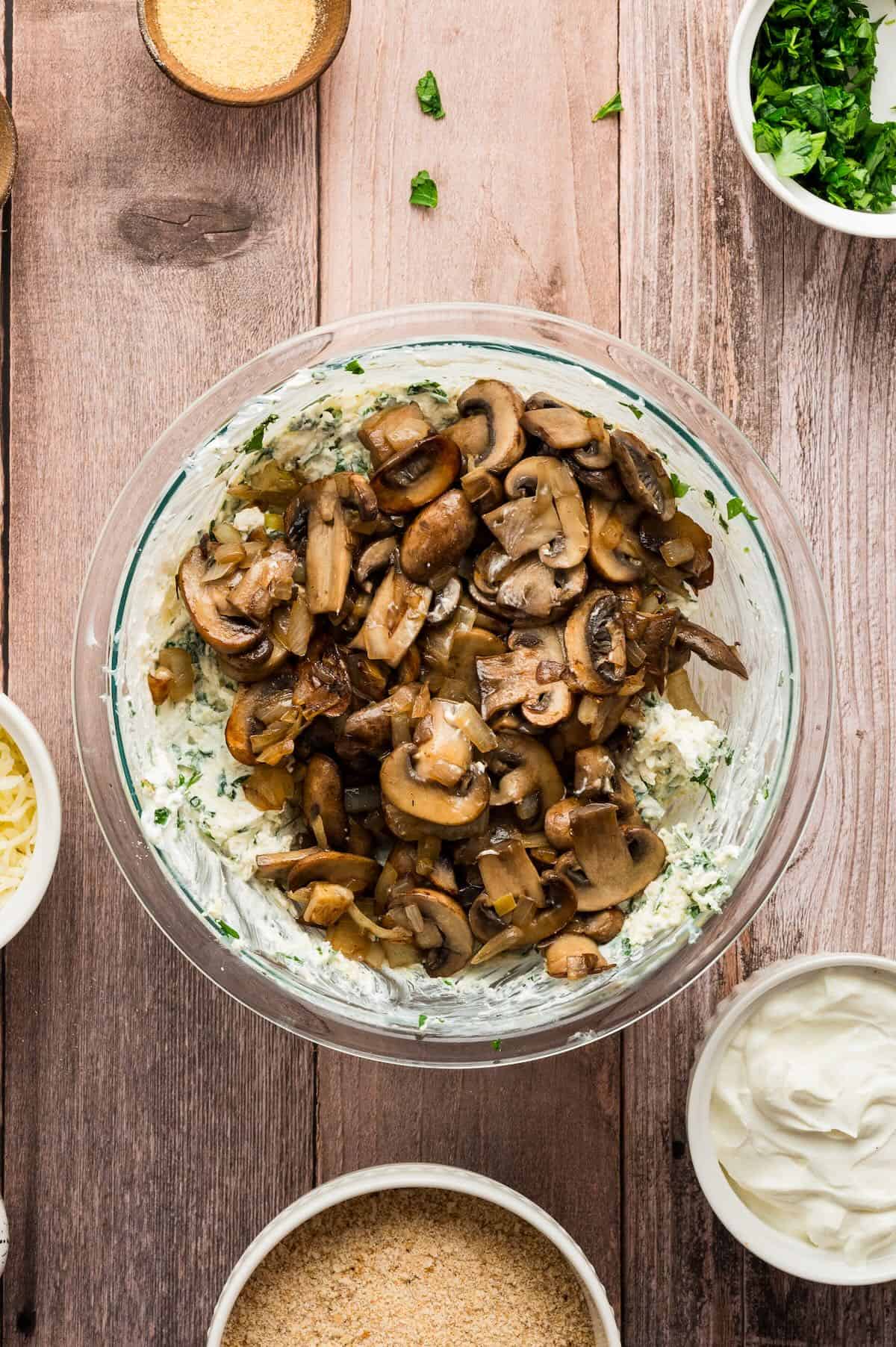 Cooked mushrooms are added to the cream cheese mixture in a bowl. 