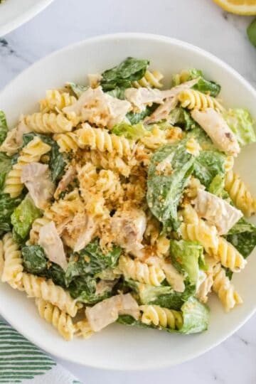 A white bowl full of chicken Caesar pasta salad topped with dressing and toasted panko.