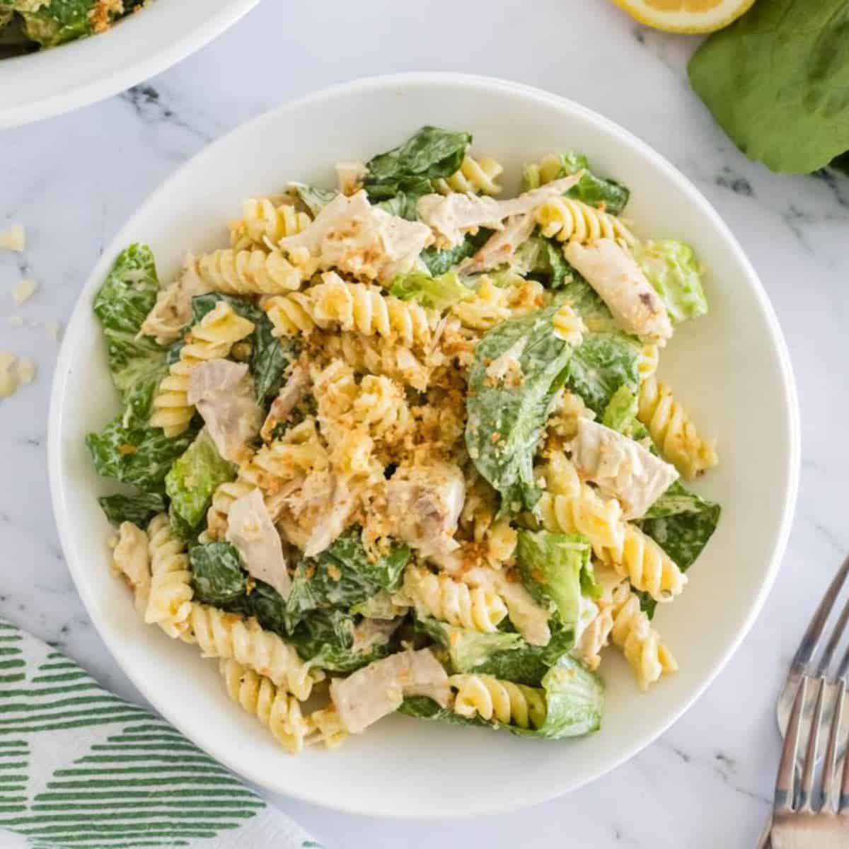 A white bowl full of chicken Caesar pasta salad topped with dressing and toasted panko.