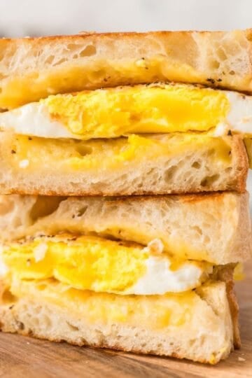 An egg and grilled cheese sandwich cut into and stacked on top of each other on a cutting board.