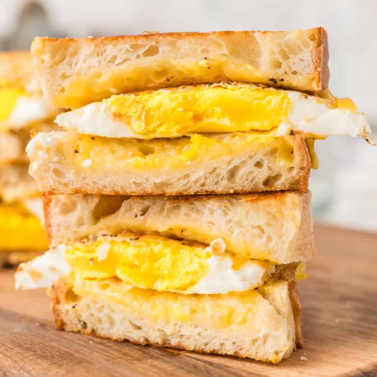 An egg and grilled cheese sandwich cut into and stacked on top of each other on a cutting board.