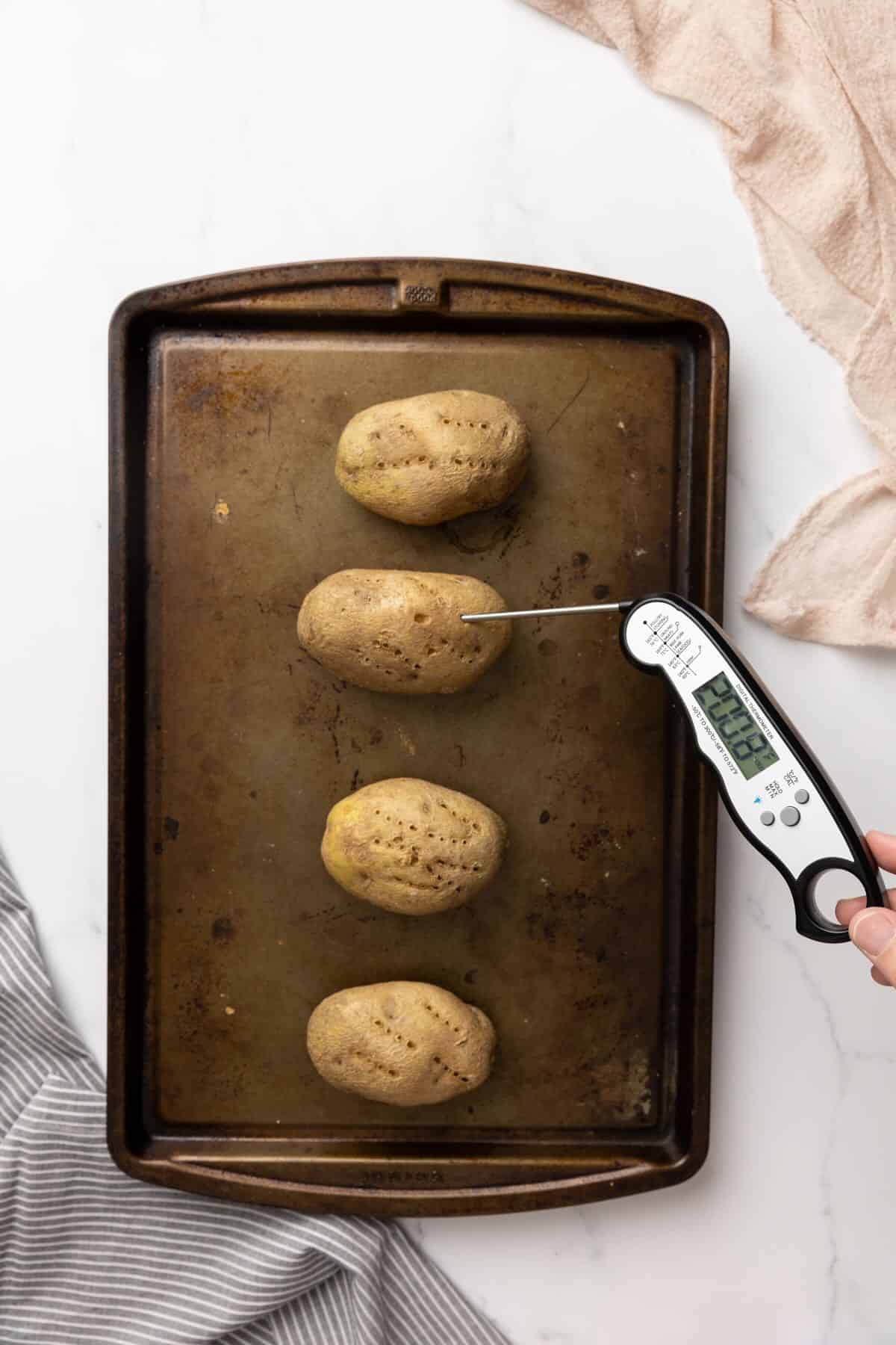 Using a meat thermometer to test the internal temperature of baked potatoes. 