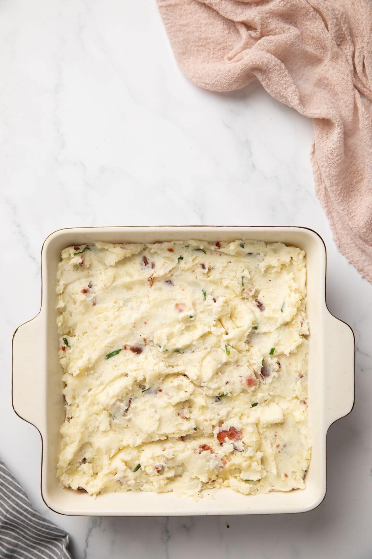 Loaded mashed potatoes in a square casserole dish, ready for the oven. 