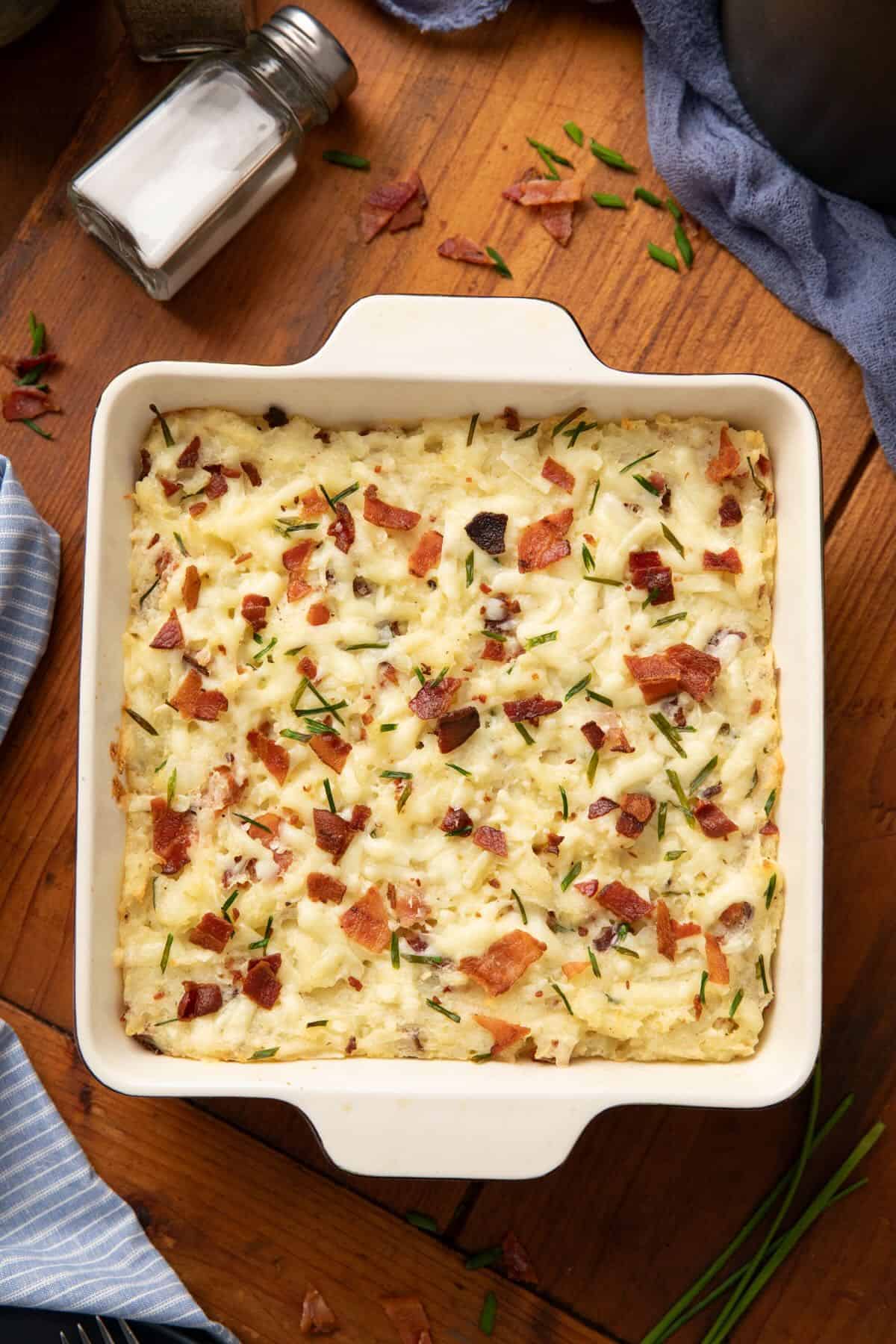Twice-baked mashed potato casserole in a square ceramic baking dish on a cutting board. 
