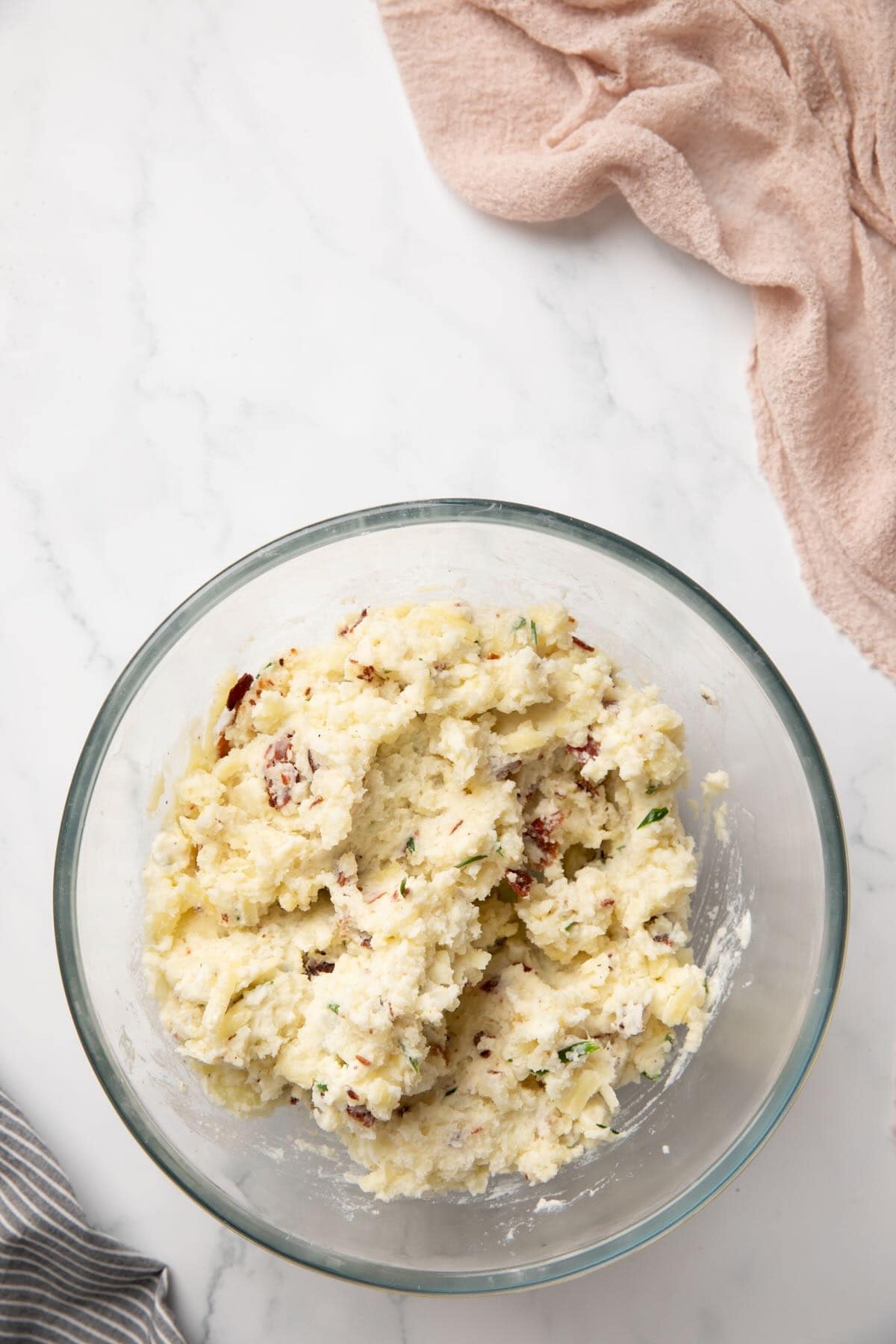 Baked mashed potatoes with chives, bacon, and cheese in a clear glass bowl.