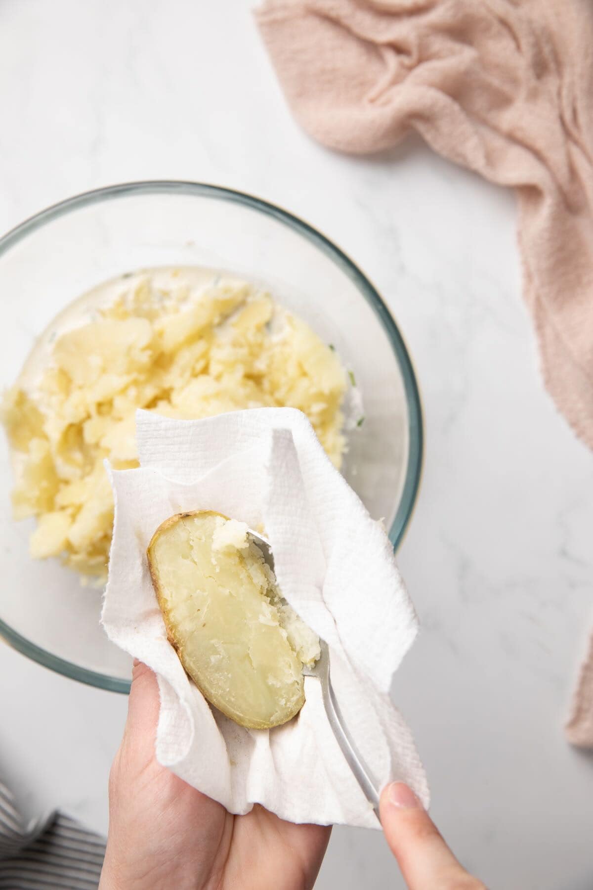Scooping out the flesh of baked potatoes into a bowl. 