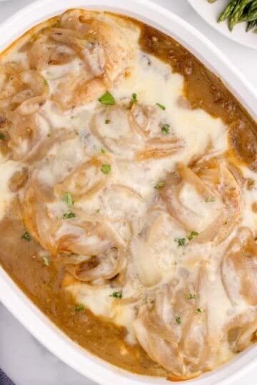 A white baking dish filled with chicken breasts in a French onion soup mixture, topped with provolone cheese.