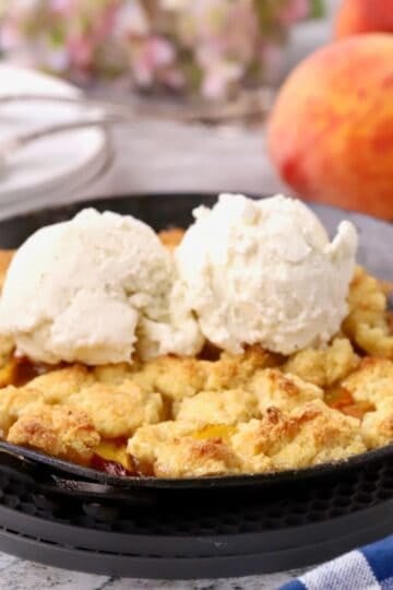 Baked small batch peach cobbler in a small cast-iron skillet topped with two scoops of vanilla ice cream.