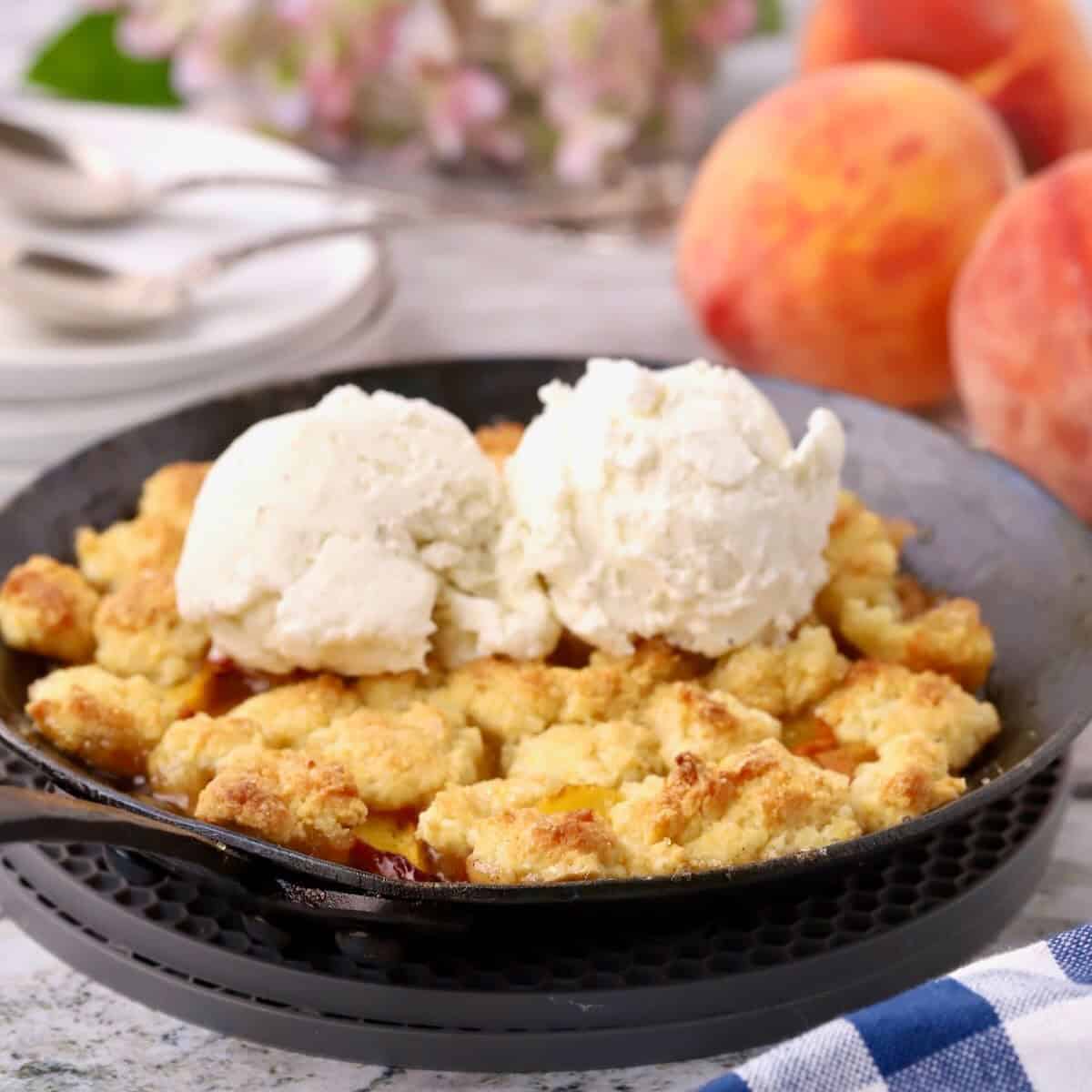 Baked small batch peach cobbler in a small cast-iron skillet topped with two scoops of vanilla ice cream.