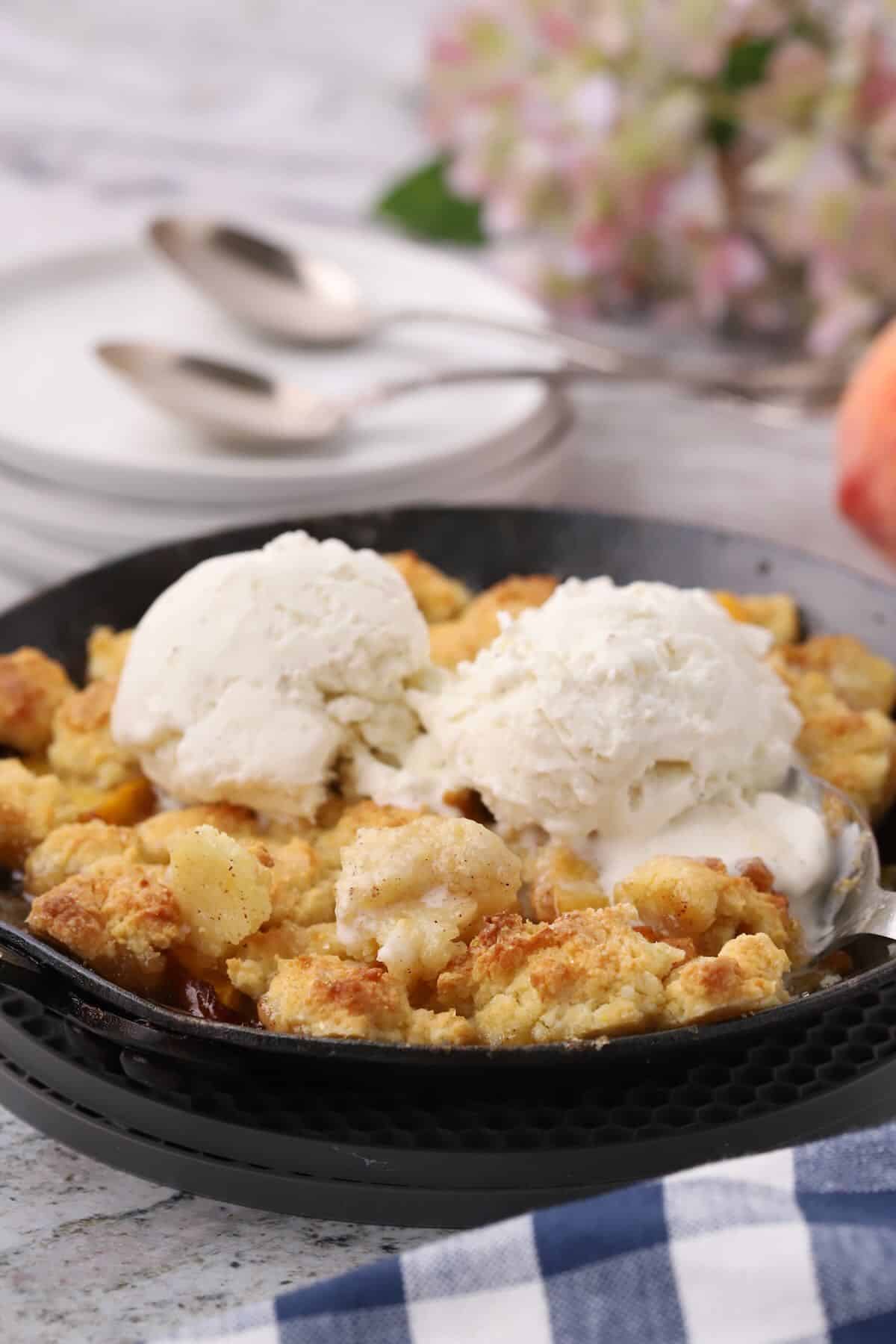 Small batch peach cobbler in a handmade cast-iron skillet topped with two scoops of ice cream.