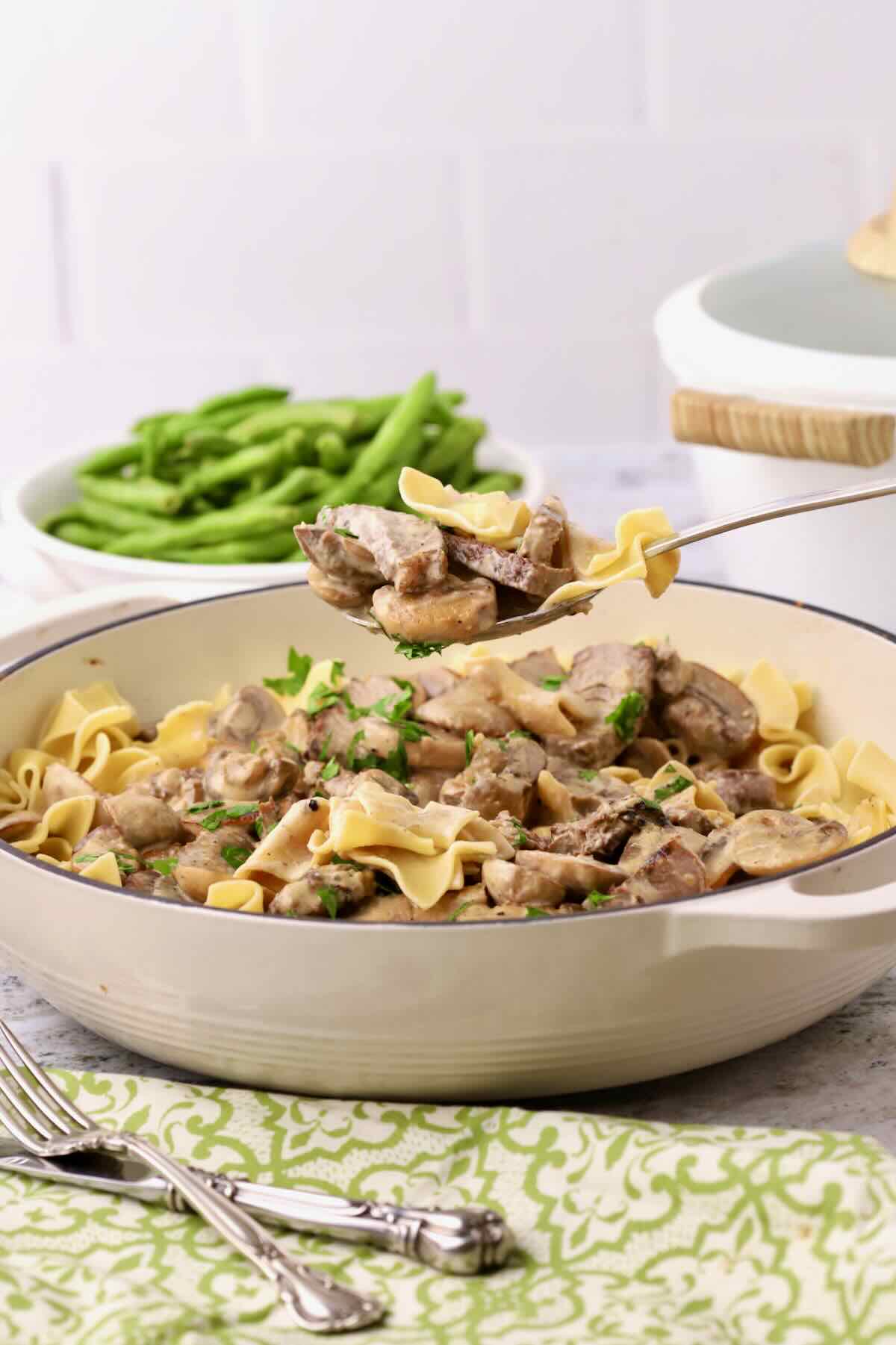 Beef Stroganoff served over egg noodles in a skillet, with a spoonful being lifted out.