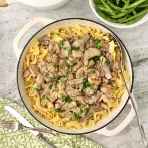 A white Dutch oven filled with beef stroganoff, made with leftover steak, served over egg noodles.