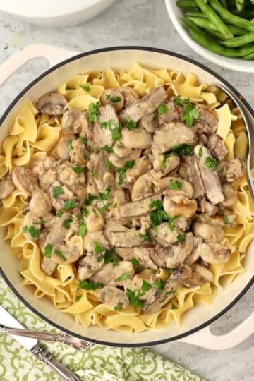 A white Dutch oven filled with beef stroganoff, made with leftover steak, served over egg noodles.