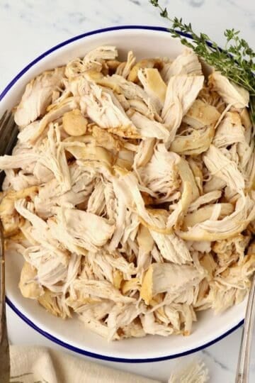 A large bowl full of Dutch Oven shredded chicken, topped with a sprig of thyme.