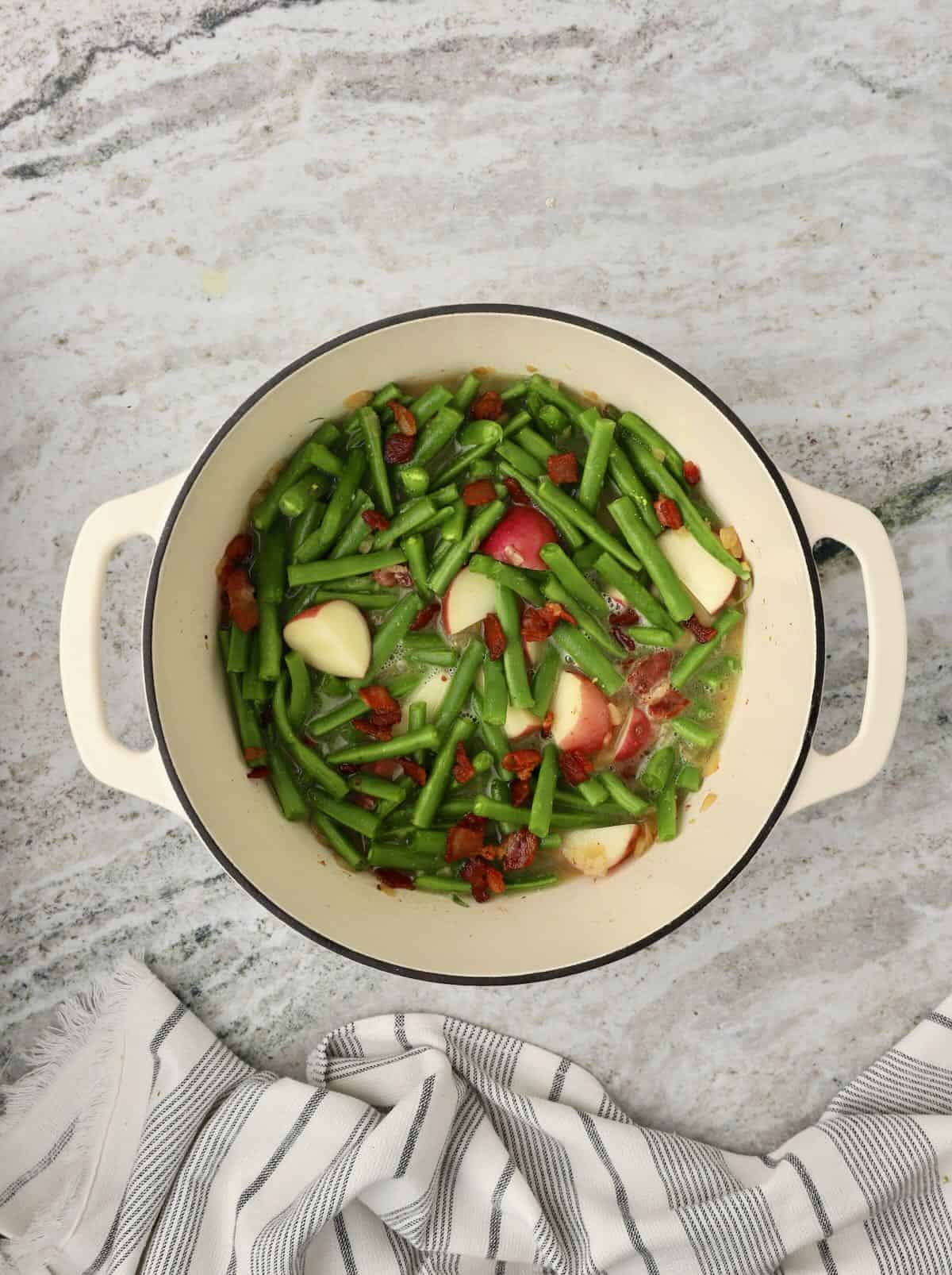 Green beans, and small red potatoes are cooking in a Dutch oven. 