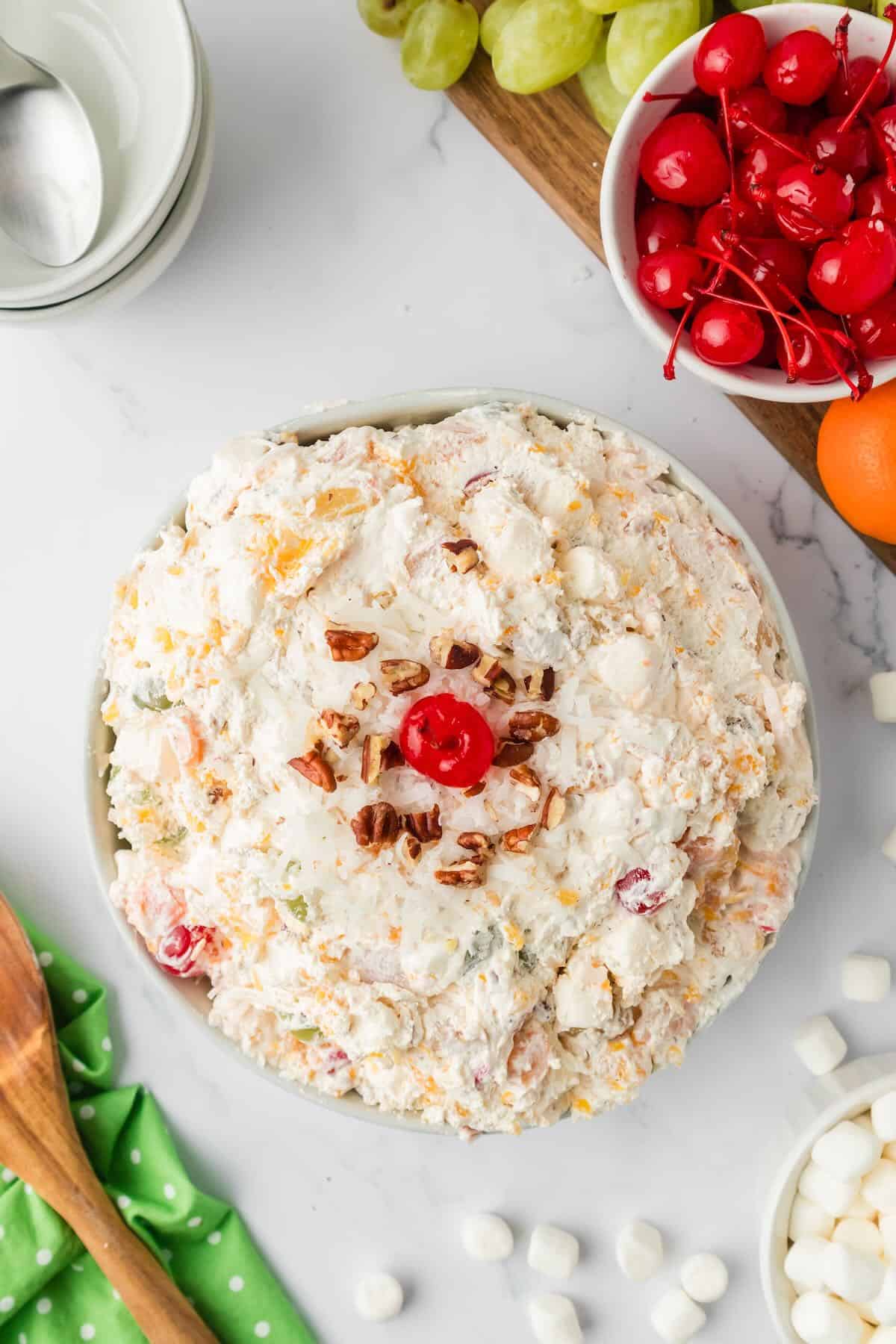 A large bowl of ambrosia fruit salad topped with chopped nuts and a cherry.