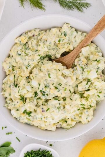 A large white bowl full of egg salad made with cottage cheese instead of mayo. There is a large wooden spoon in the bowl.