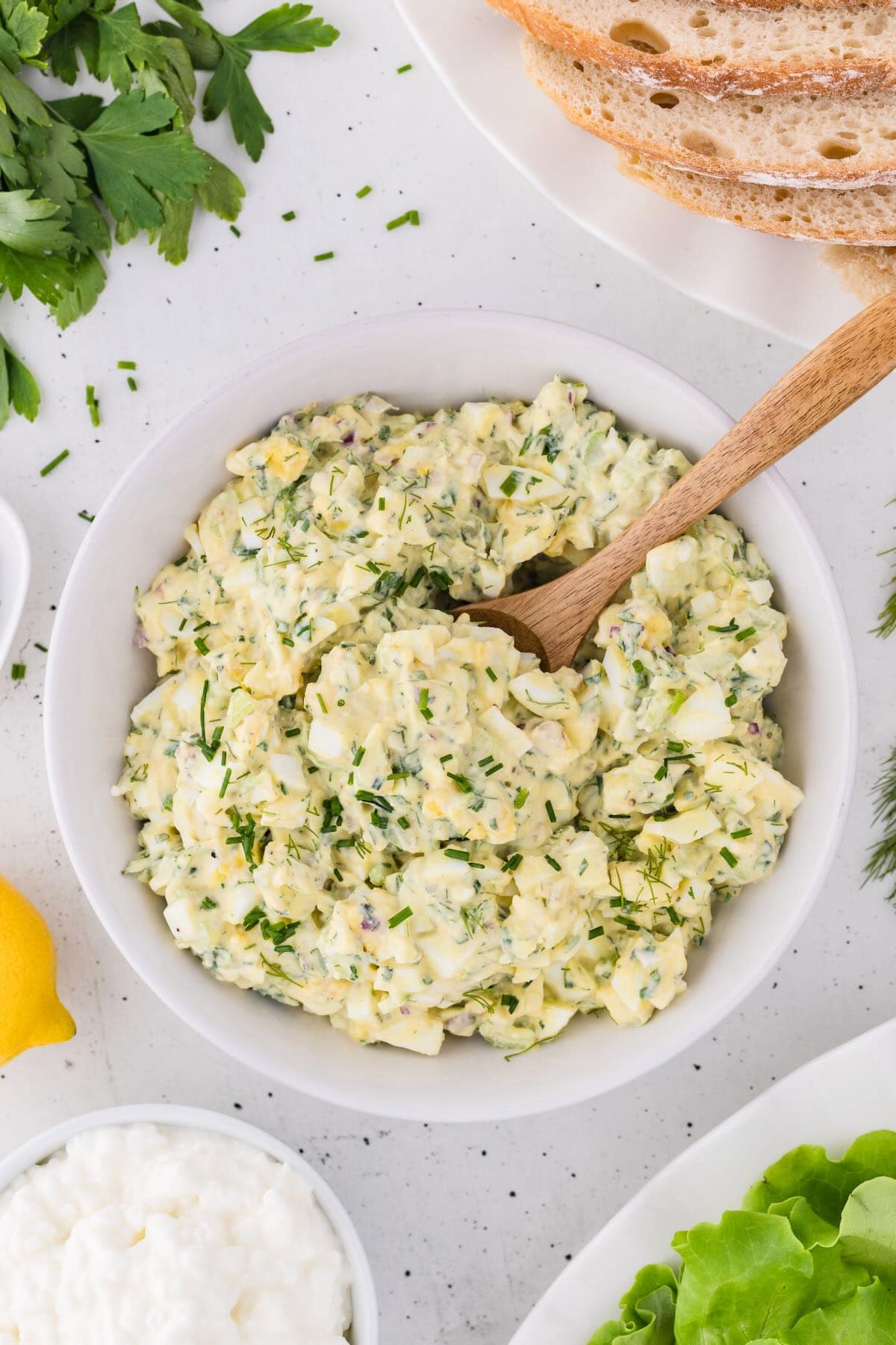 A large white bowl full of egg salad with a wooden spoon.