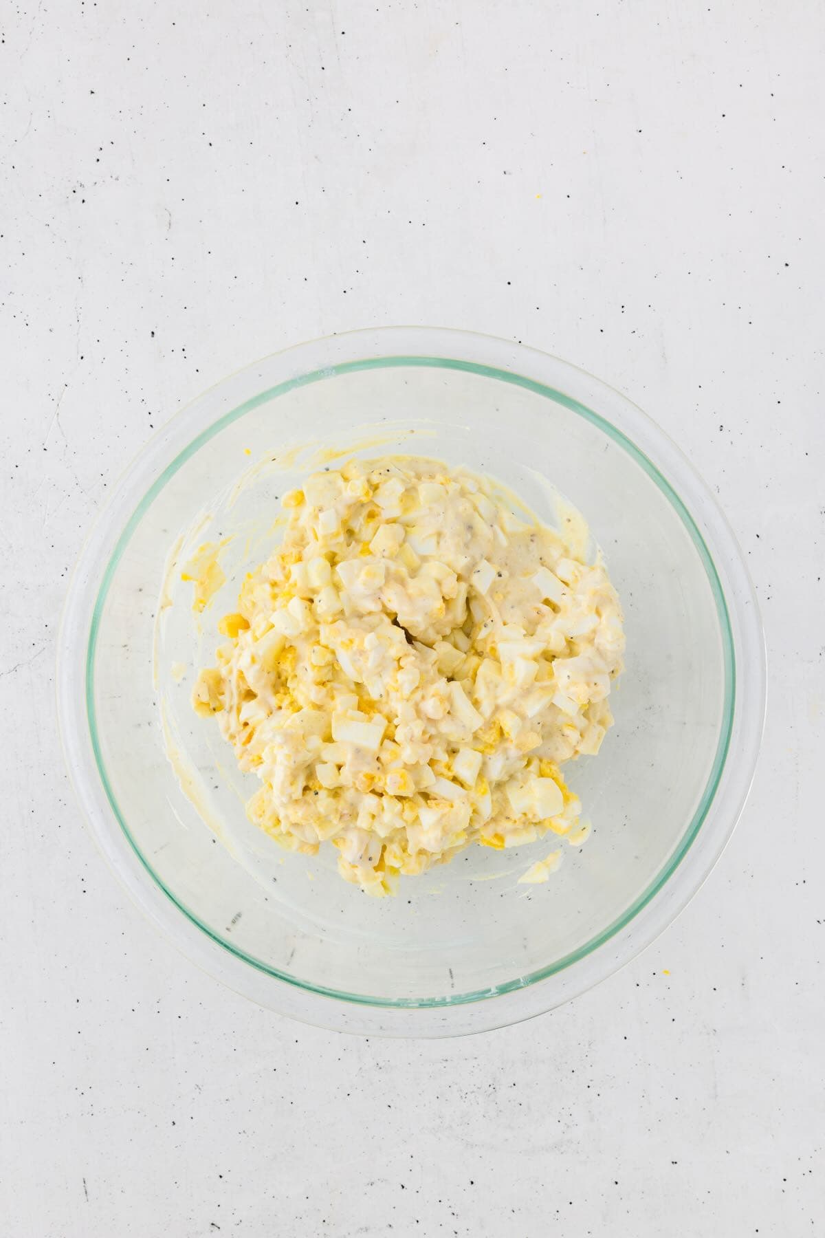 Chopped eggs and cottage cheese sauce are mixed together in a bowl.