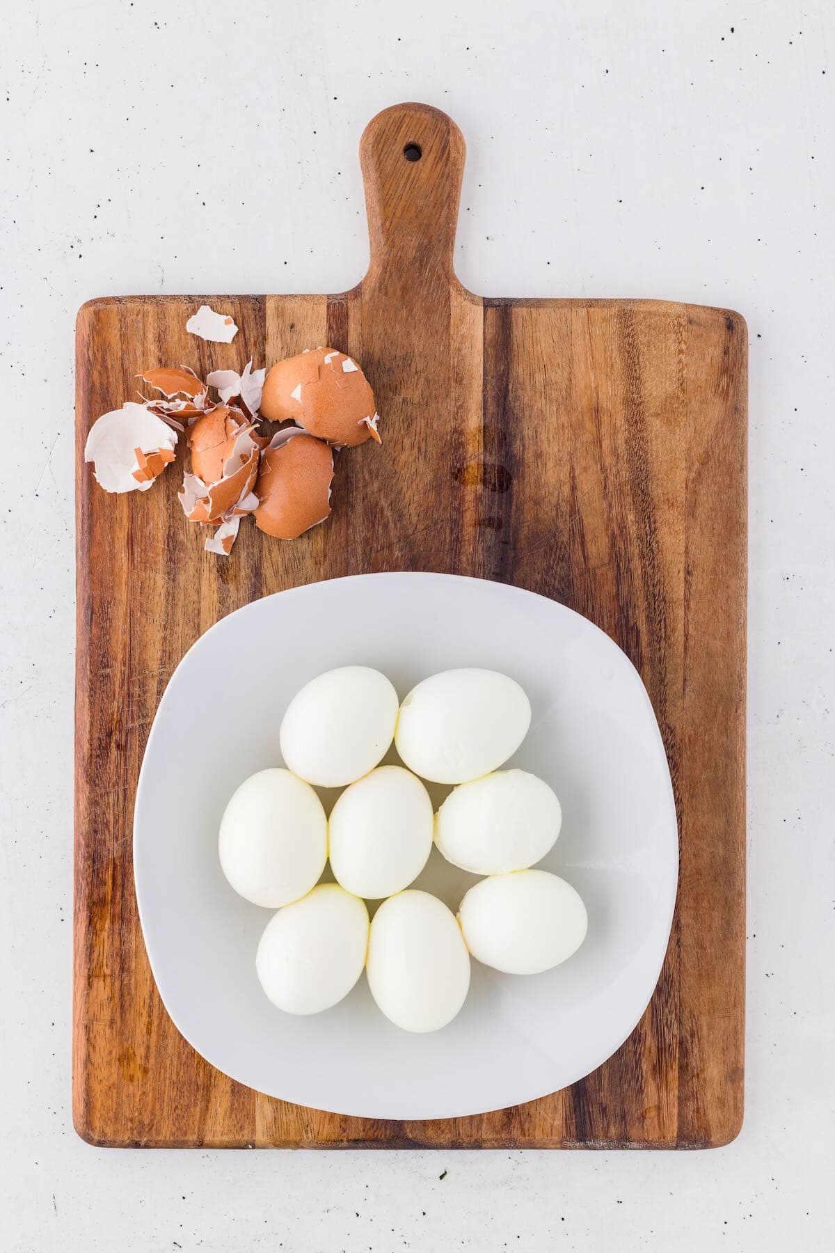 Eight peeled eggs on a plate on a cutting board.