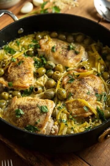 A skillet with cooked Mediterranean Chicken and Orzo using chicken thighs, plus olives and preserved lemon.