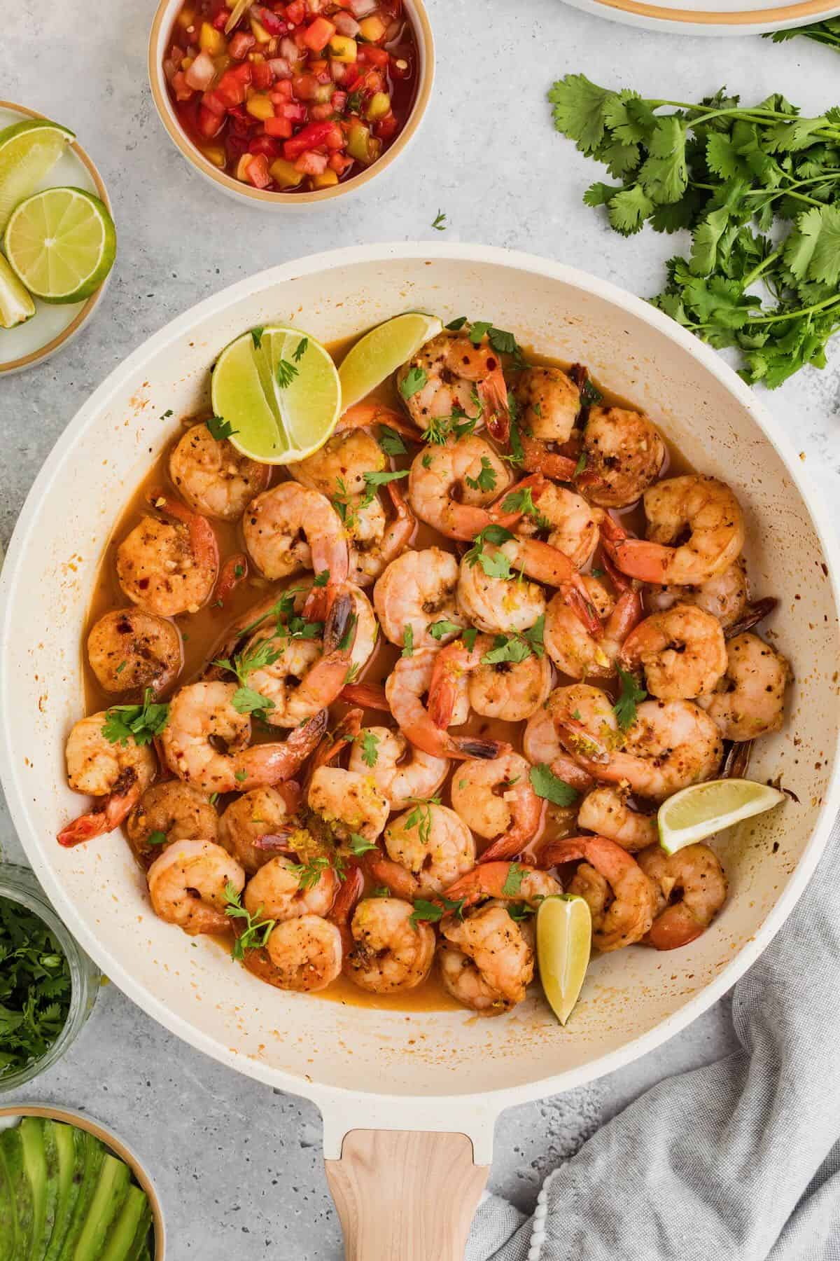 Cooked Tequila Lime Shrimp in a skillet, garnished with lime slices and cilantro. 