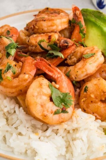 Horizontal plate of tequila lime shrimp served over white rice, garnished with avocado slices, cilantro, and fresh lime wedges.