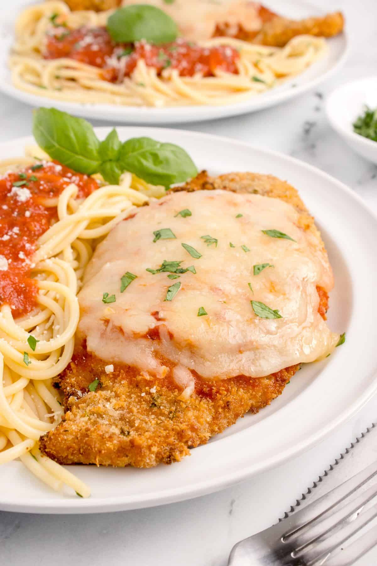 A parmesan crusted chicken breast topped with melted mozzarella cheese and spaghetti sauce on a plate.