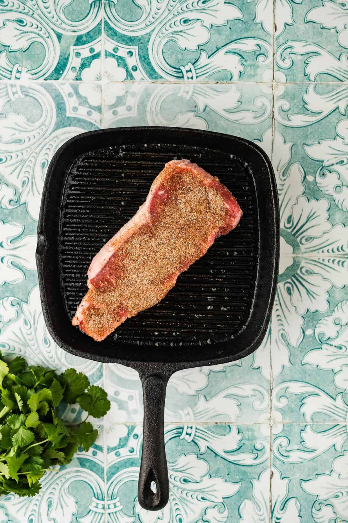 A steak is cooking on the stove in a grill pan.