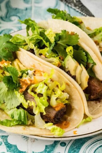 Three sirloin steak tacos topped with chipotle crema and cilantro.