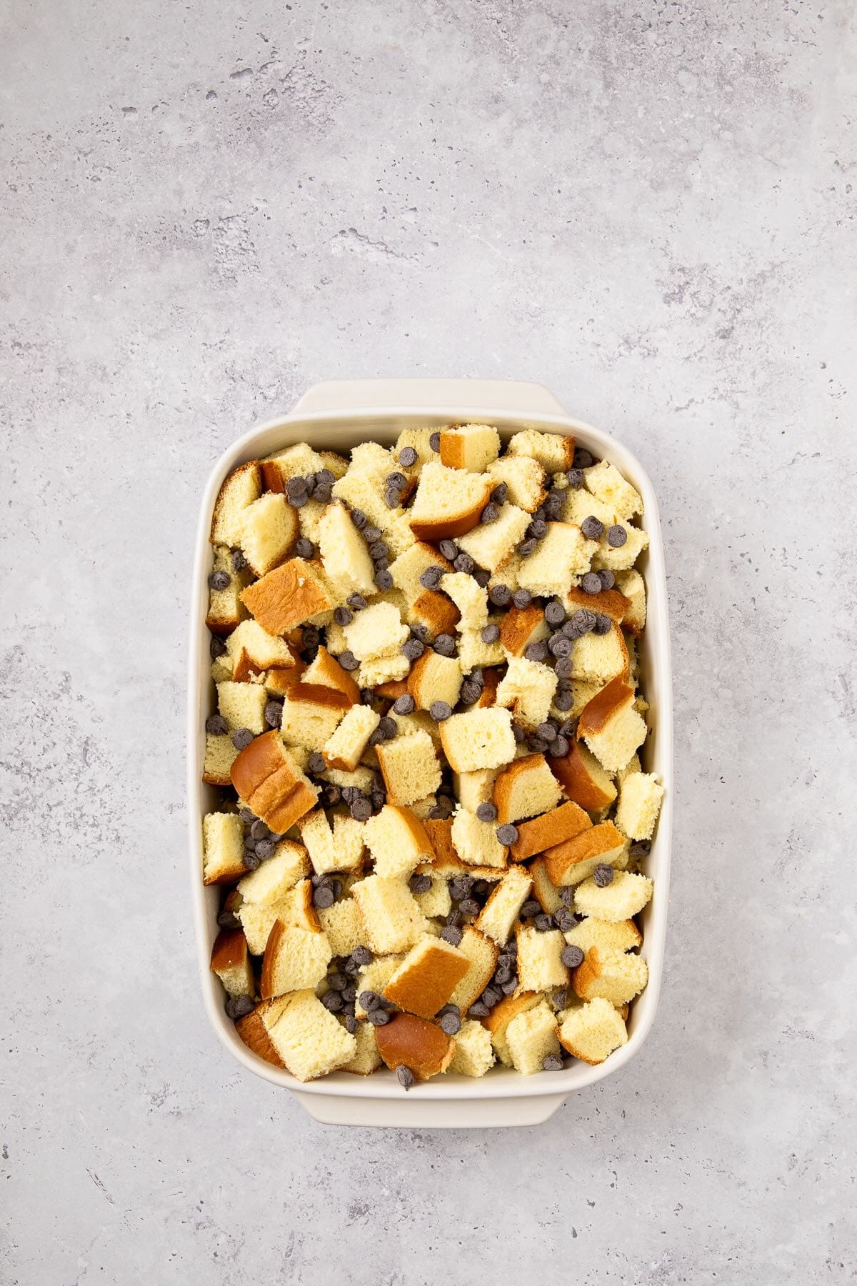 A rectangular baking dish full of bread cubes and chocolate chips.