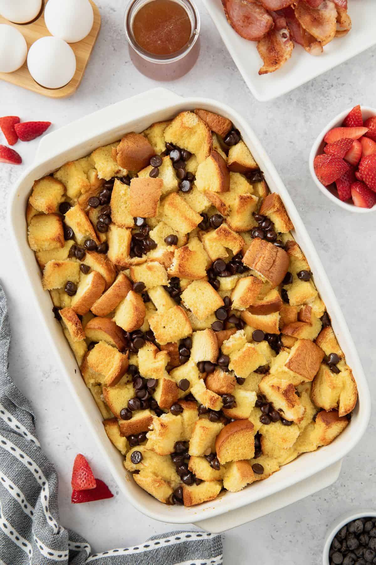 A white baking dish full of baked french toast brioche with chocolate chips.