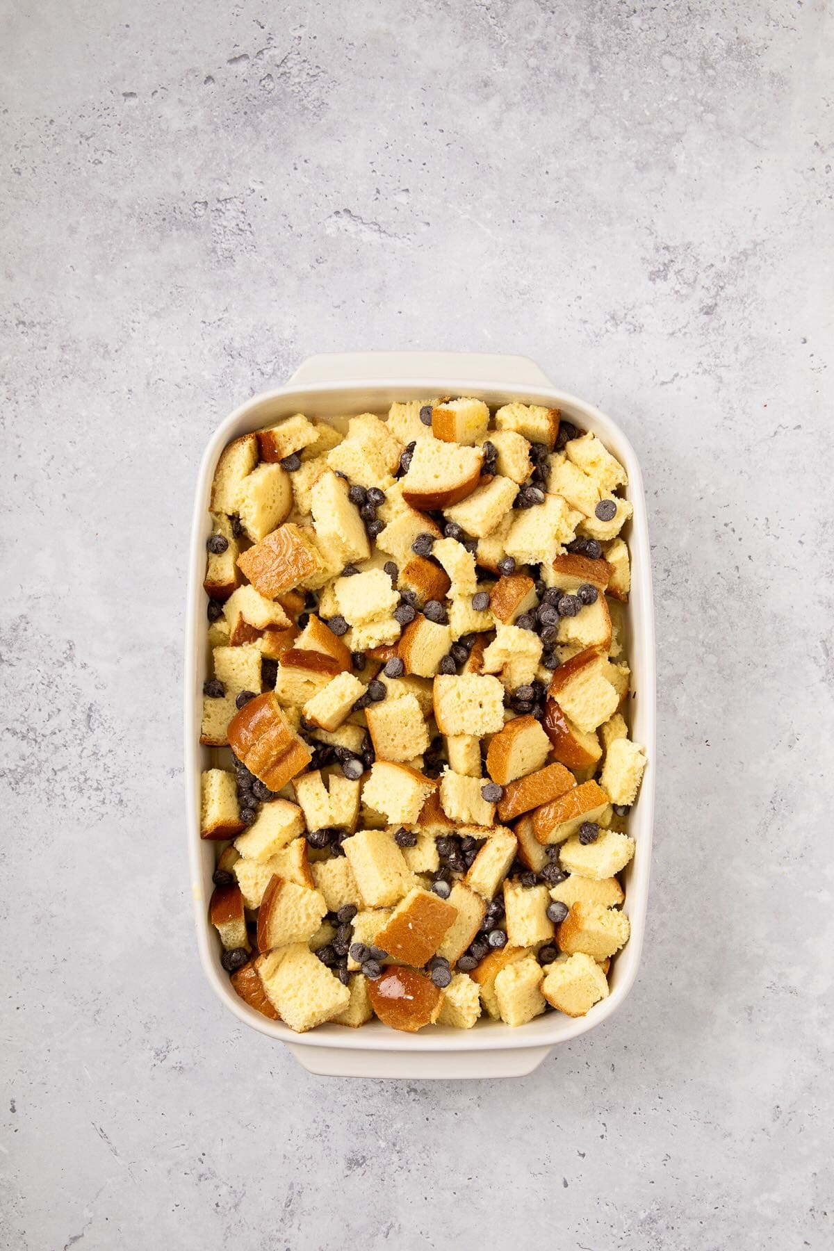 Cubes of brioche bread and chocolate chips soaking in custard in preparation for baking.