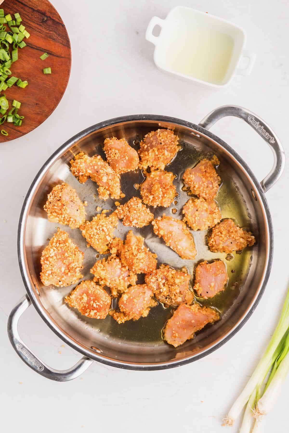 Chicken coated in egg, then panko, cooking in a skillet.