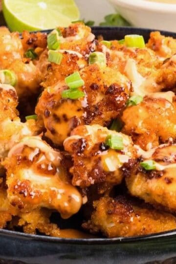 A platter of bang bang chicken topped with bang bang sauce and chopped scallions.