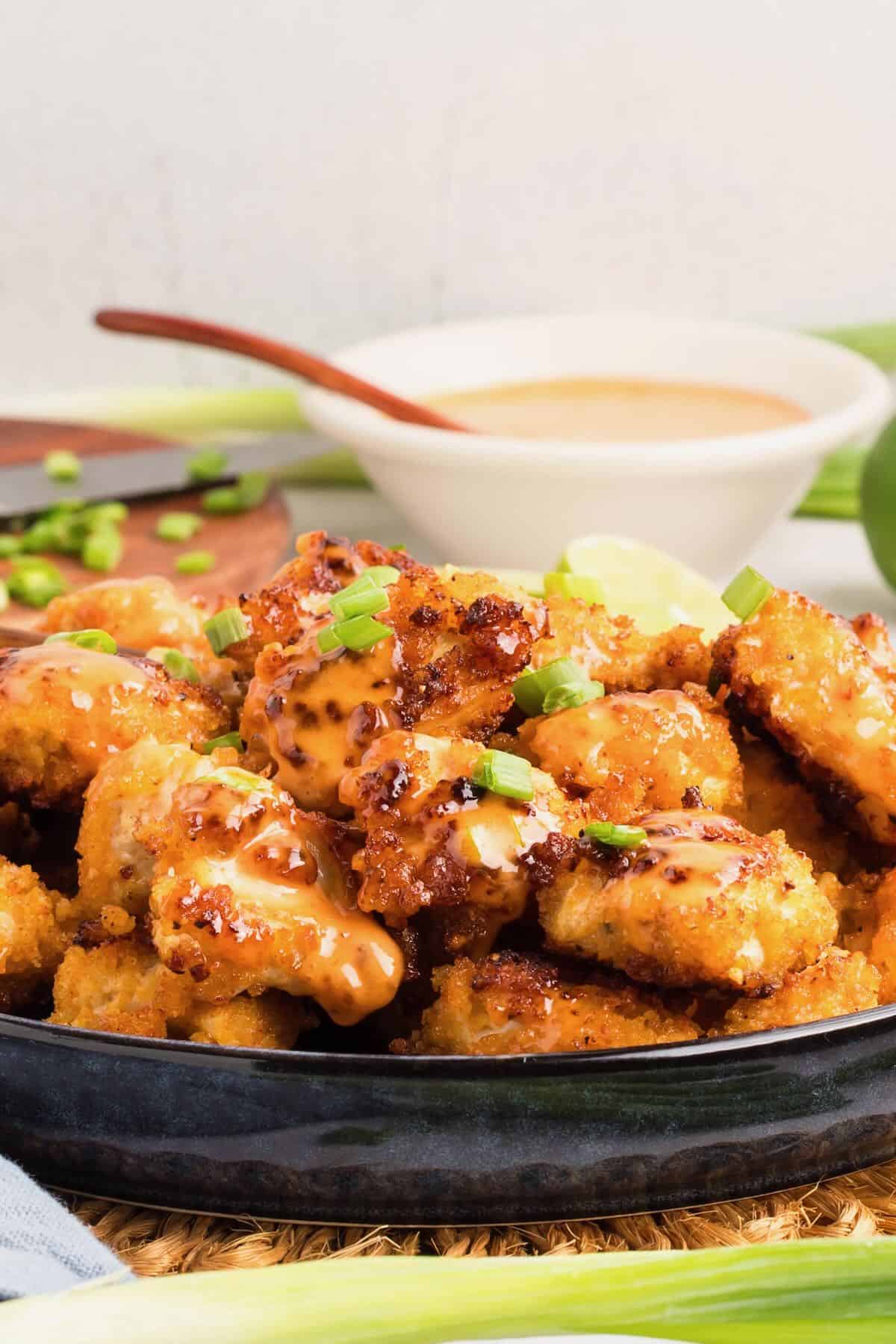 Bang bang chicken with sauce on a platter, garnished with chopped scallions.