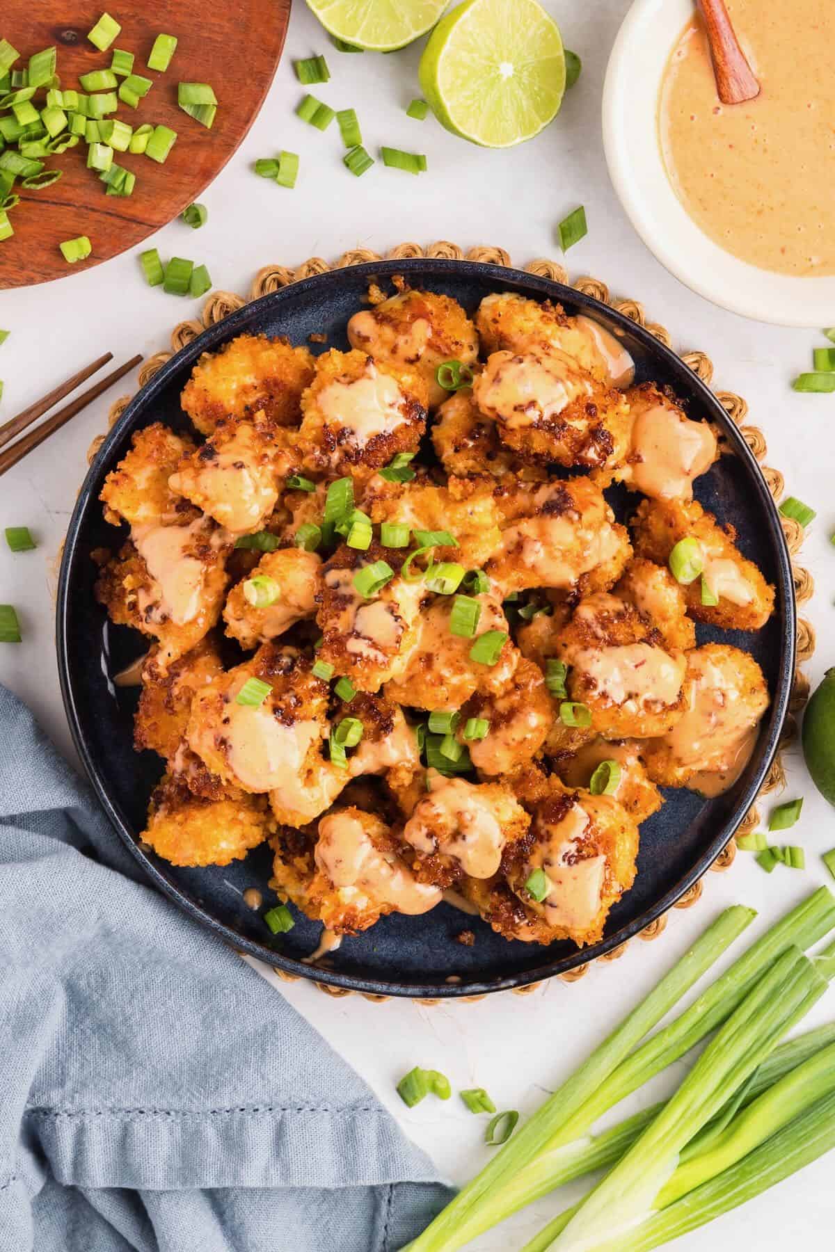 A plate full of crispy bang bang chicken topped with bang bang sauce and garnished with scallions.