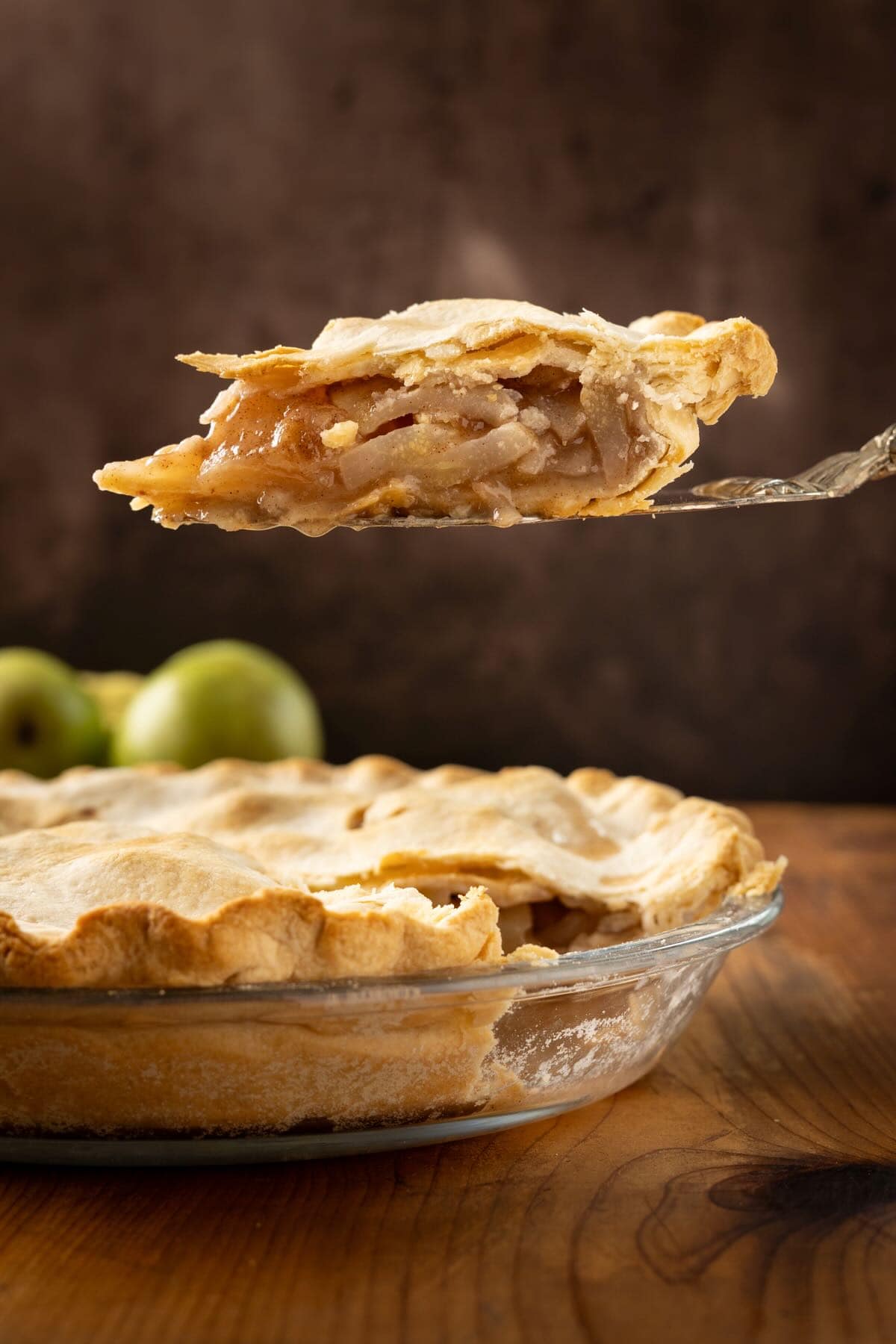 A slice of pear pie held over the whole pie with pears in the background. 