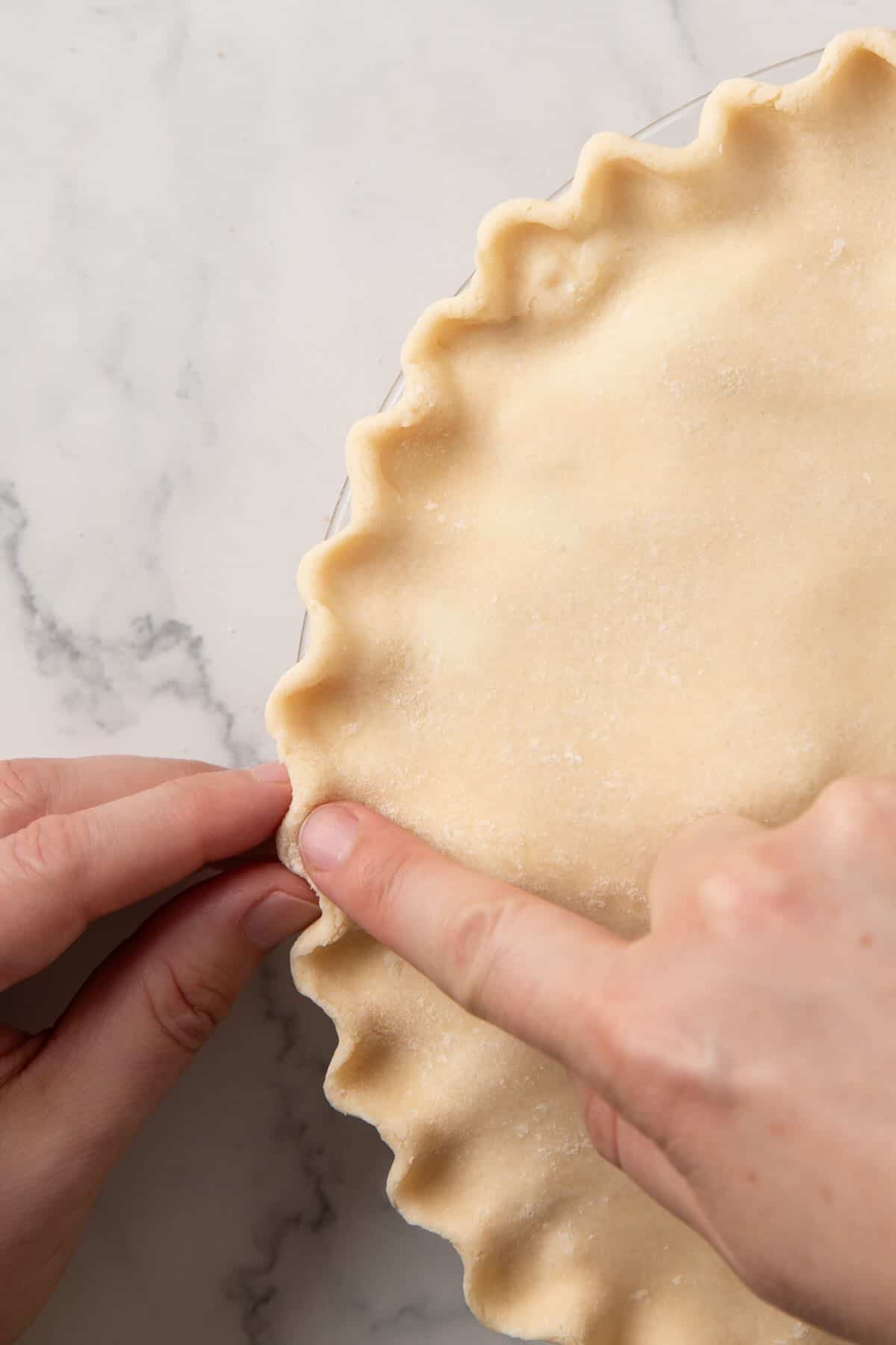 A close-up shot showing how to use your fingers to flute a pie crust. 