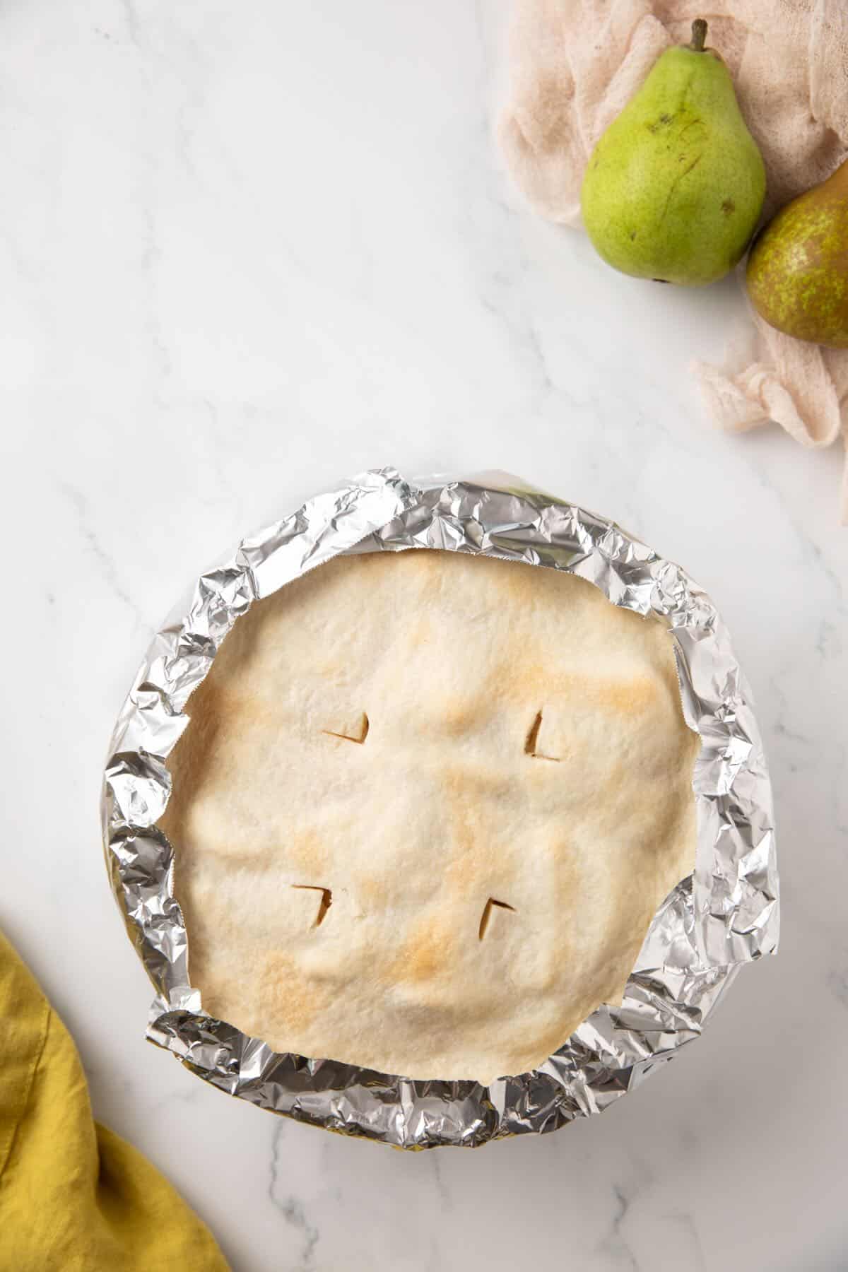 A pear pie partially baked with strips of foil over the edges to prevent them from burning. 