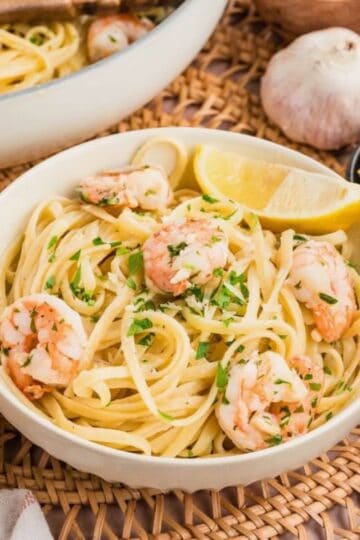 A bowl of shrimp scampi garnished with a lemon slice and chopped parsley.